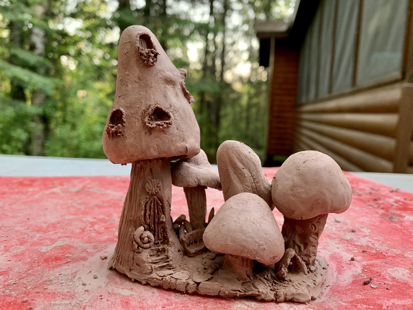 Clay mushroom house sculpture — tall toadstool with windows, a tiny door with snail, and three smaller mushrooms beside it