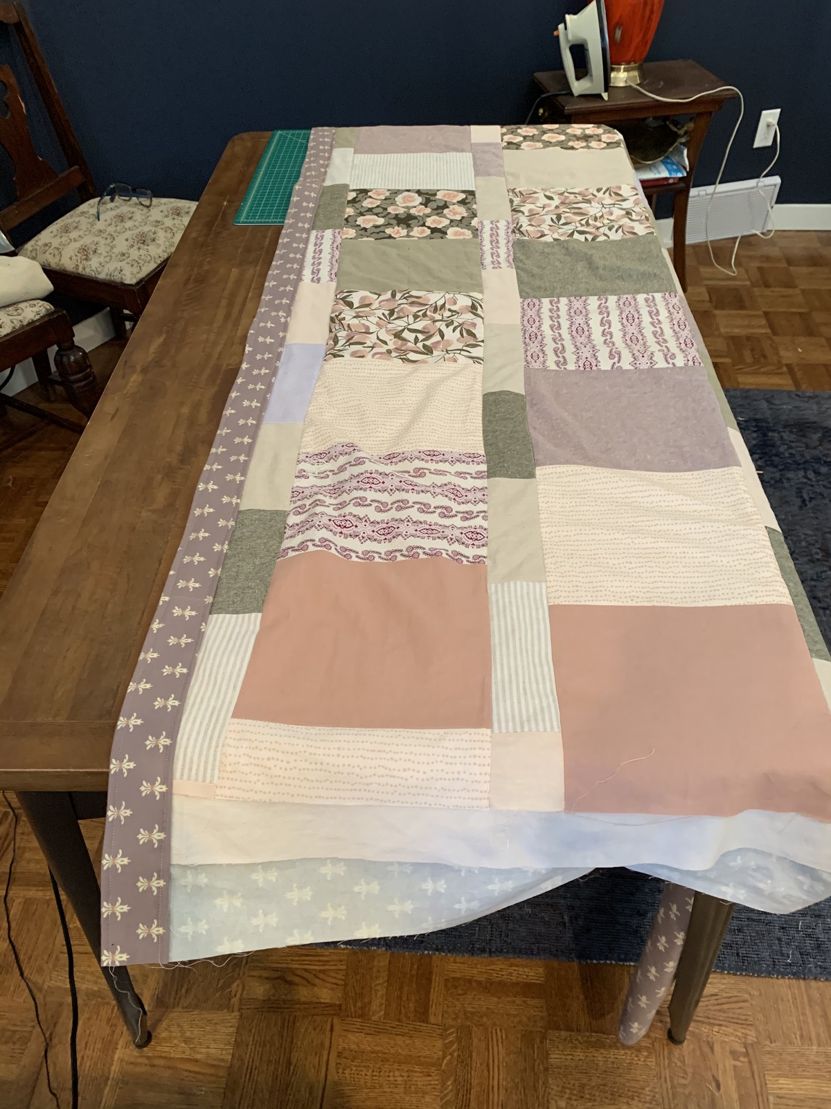 Dear Momma quilt laid out on a table — patchwork blocks of pink, sage, grey, paisley, and floral prints with mauve fleur-de-lis border