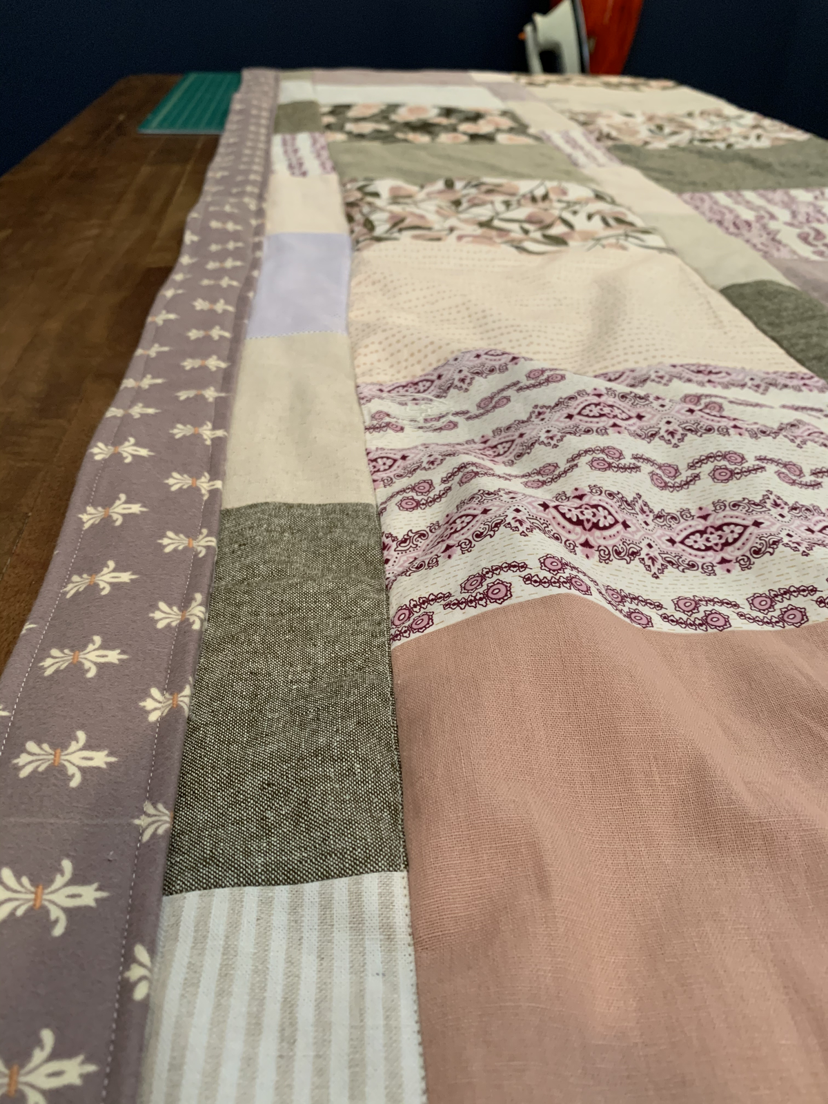 Close view of Dear Momma quilt — sage green, paisley print, blush and striped blocks beside the mauve border