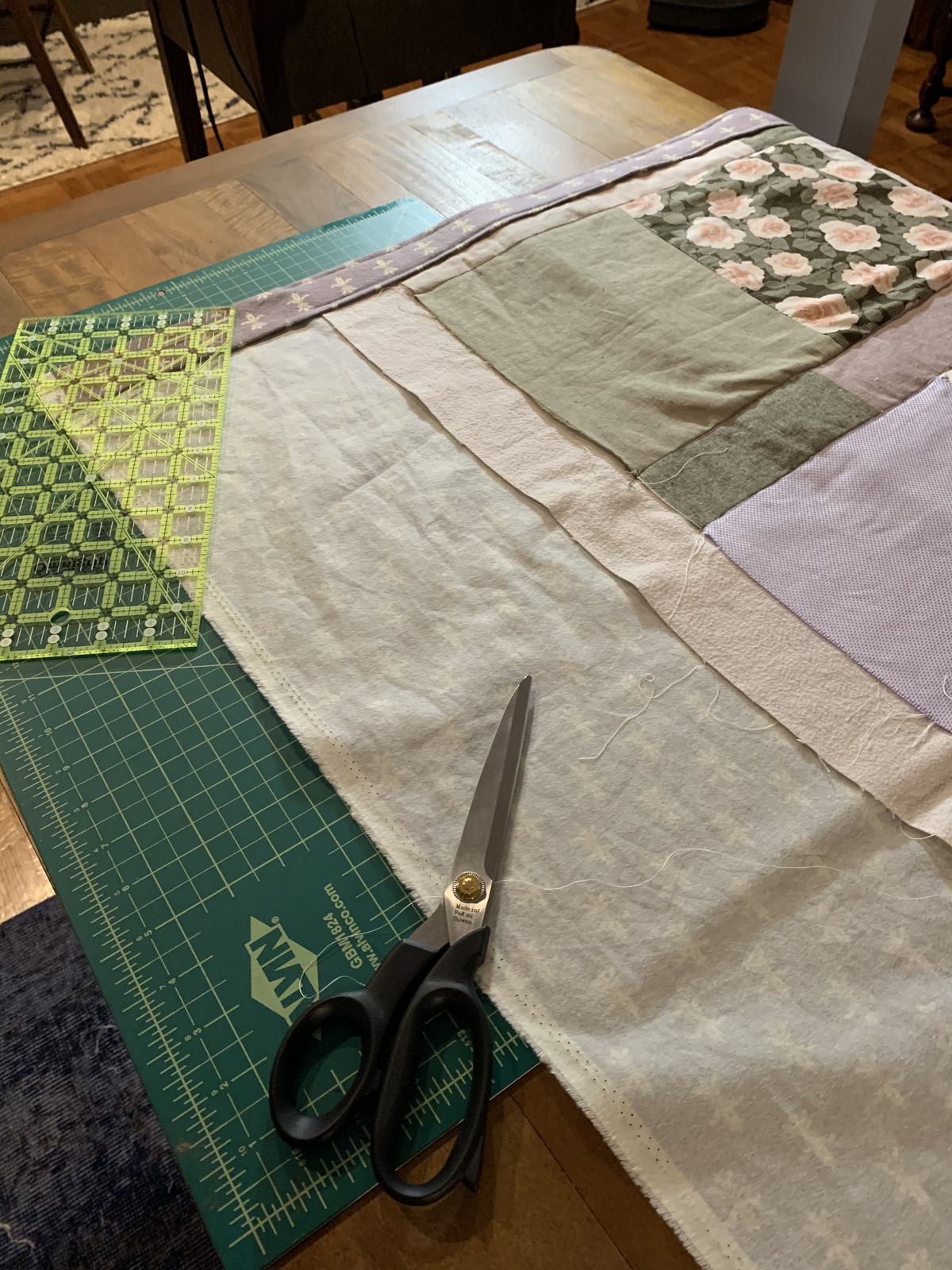 Dear Momma quilt backing visible with cutting mat and scissors — cream fabric with subtle pattern beside green and floral blocks