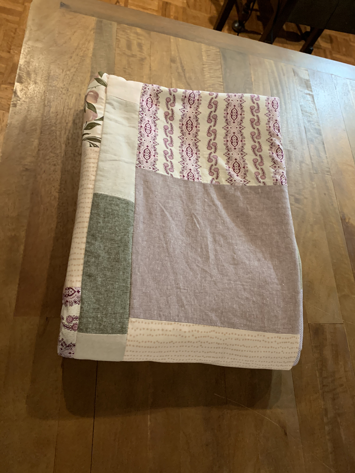 Dear Momma quilt folded on hardwood — paisley print, sage green, lavender, and dotted cream blocks