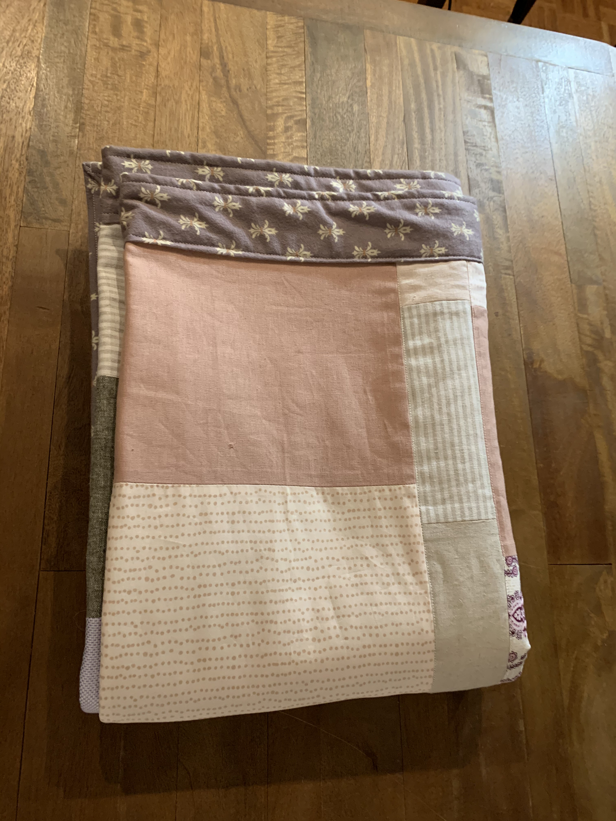 Dear Momma quilt folded — blush pink, mauve border, striped, and dotted cream blocks on hardwood floor