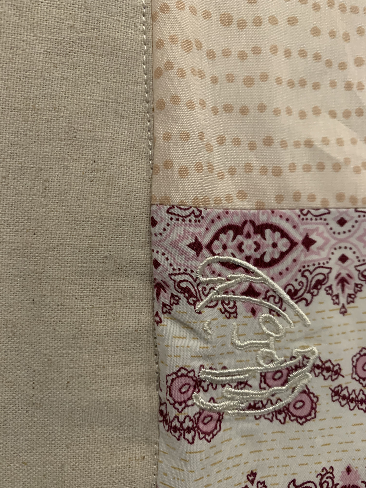 Close detail of Dear Momma quilt — embroidered motif in white thread on paisley and dotted fabric at block seam
