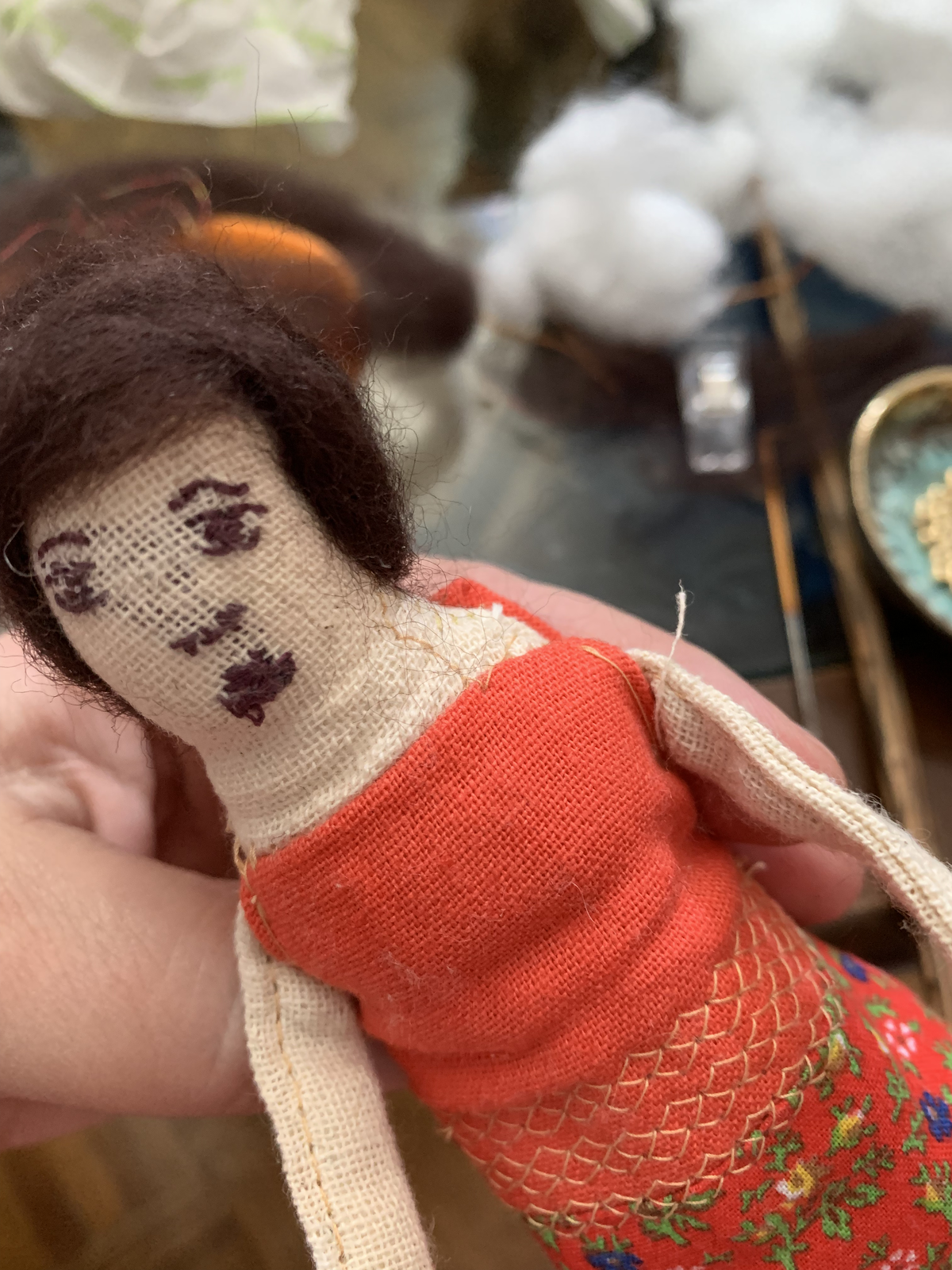 Close-up of genealogy doll — embroidered face detail and red bodice
