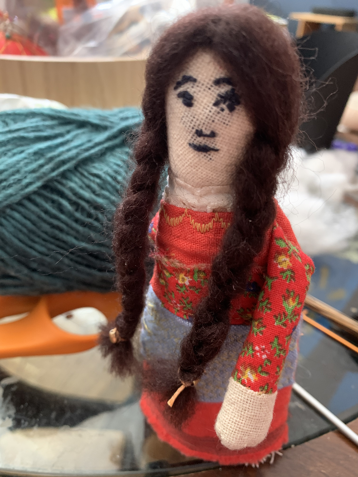 Genealogy doll with long dark braids, red floral dress, lavender apron, and linen boots
