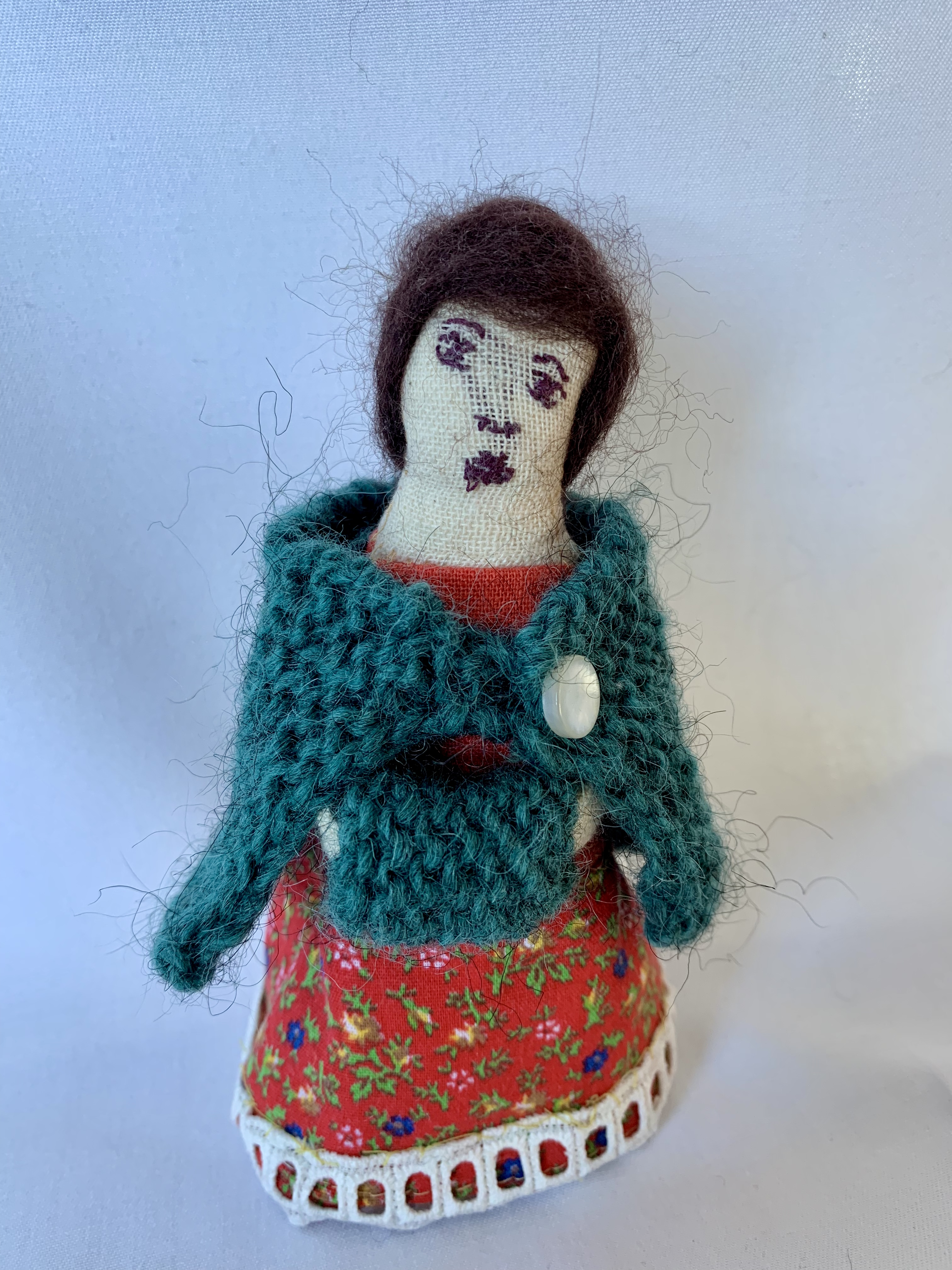 Genealogy doll in red floral dress with teal knitted cardigan and white button