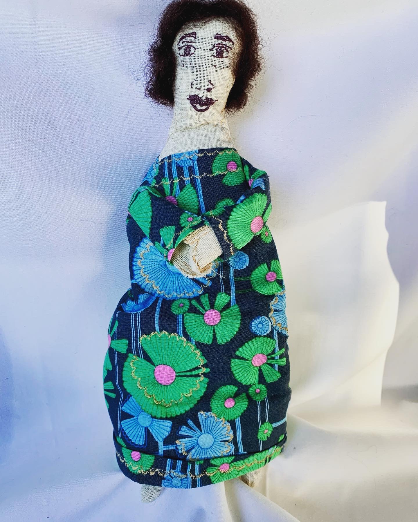 Genealogy doll in green and blue floral print dress with embroidered face and dark wool hair