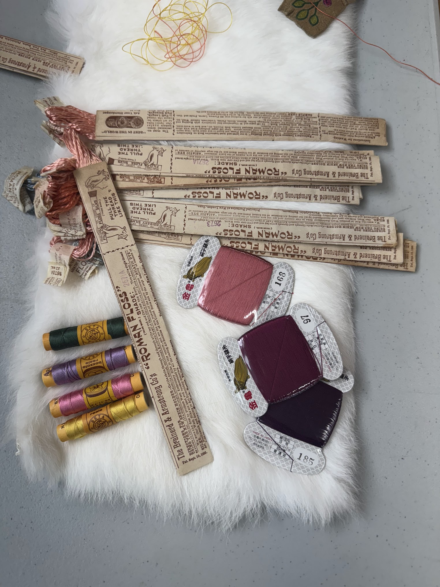 Vintage Roman Floss packaging, silk spools, and thread cards on white fur