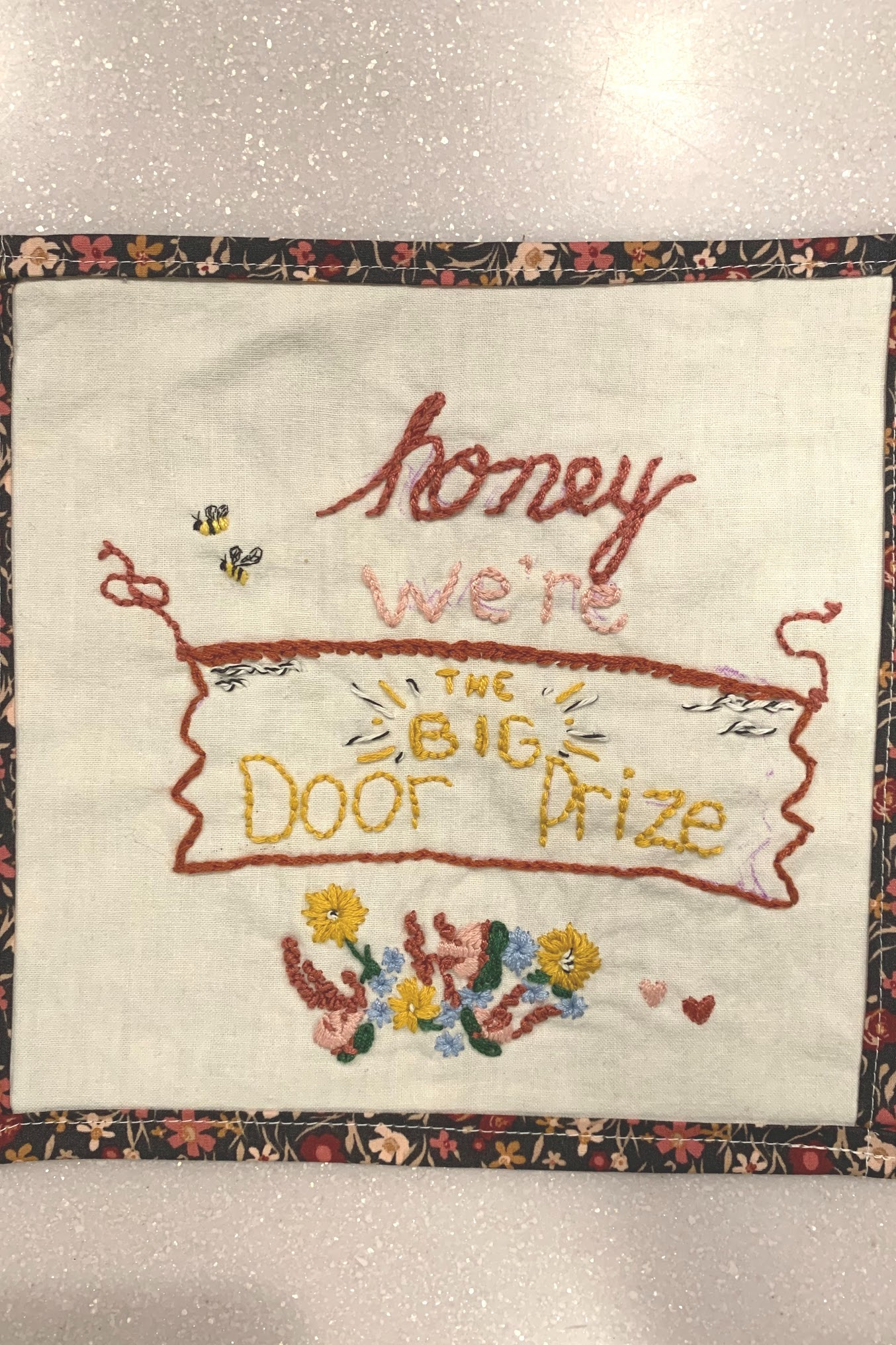 Hand embroidery on linen with floral border — 'honey we're THE BIG Door Prize' stitched in red and gold with bees and flowers