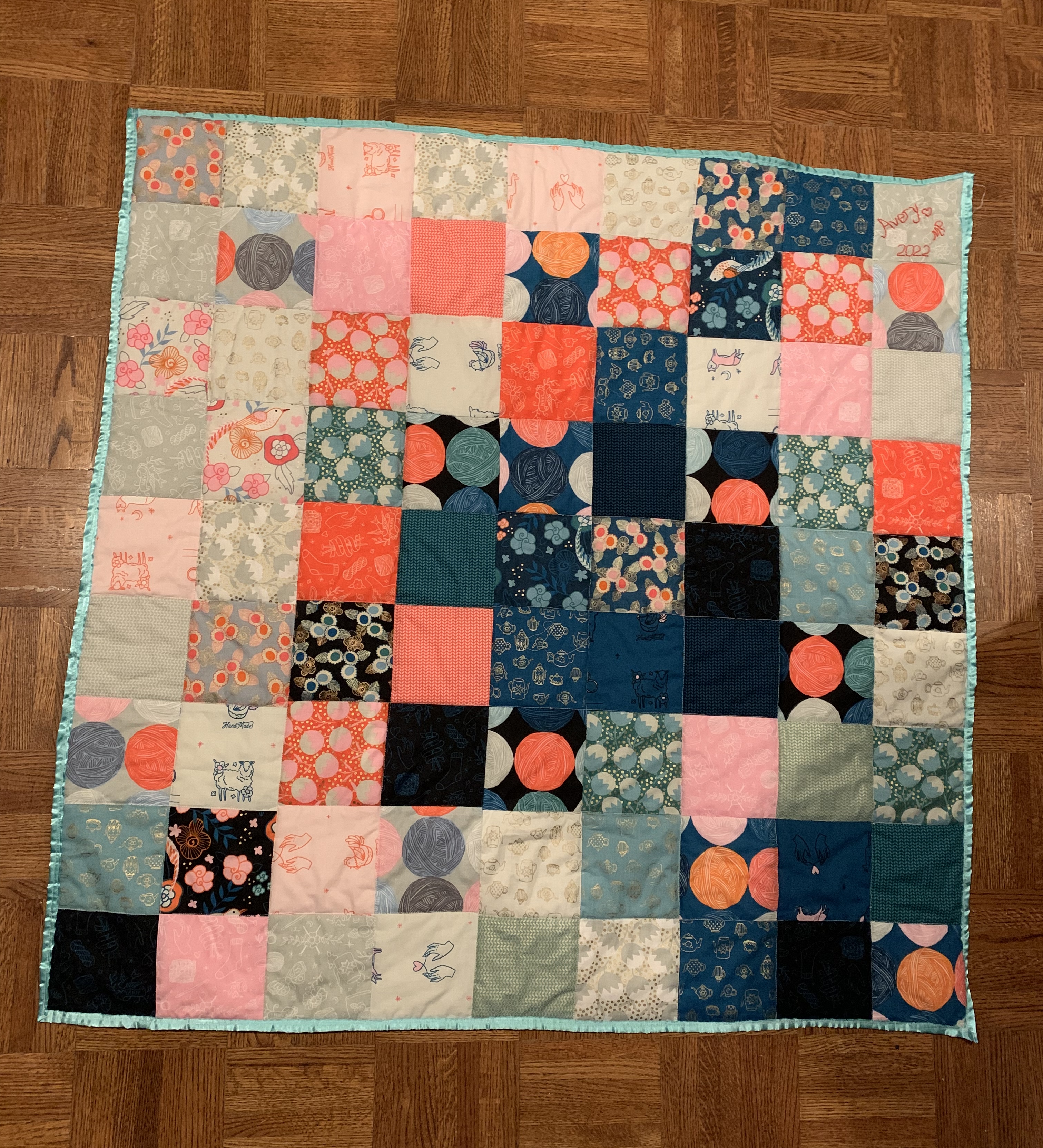 Little Fire quilt — patchwork of coral, navy, teal, grey, and pink squares with yarn ball and cat prints, aqua satin binding