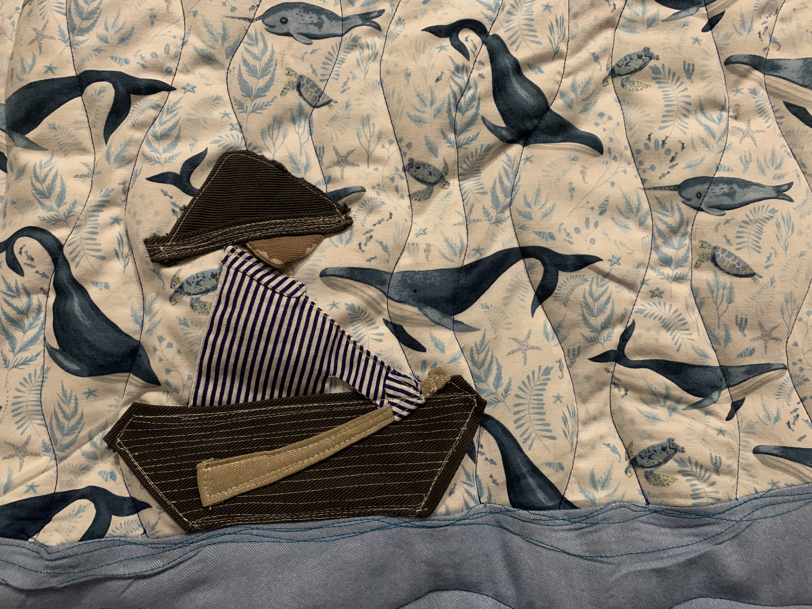 Close detail — appliqué boat pieces laid out on whale print fabric beside blue wave quilting