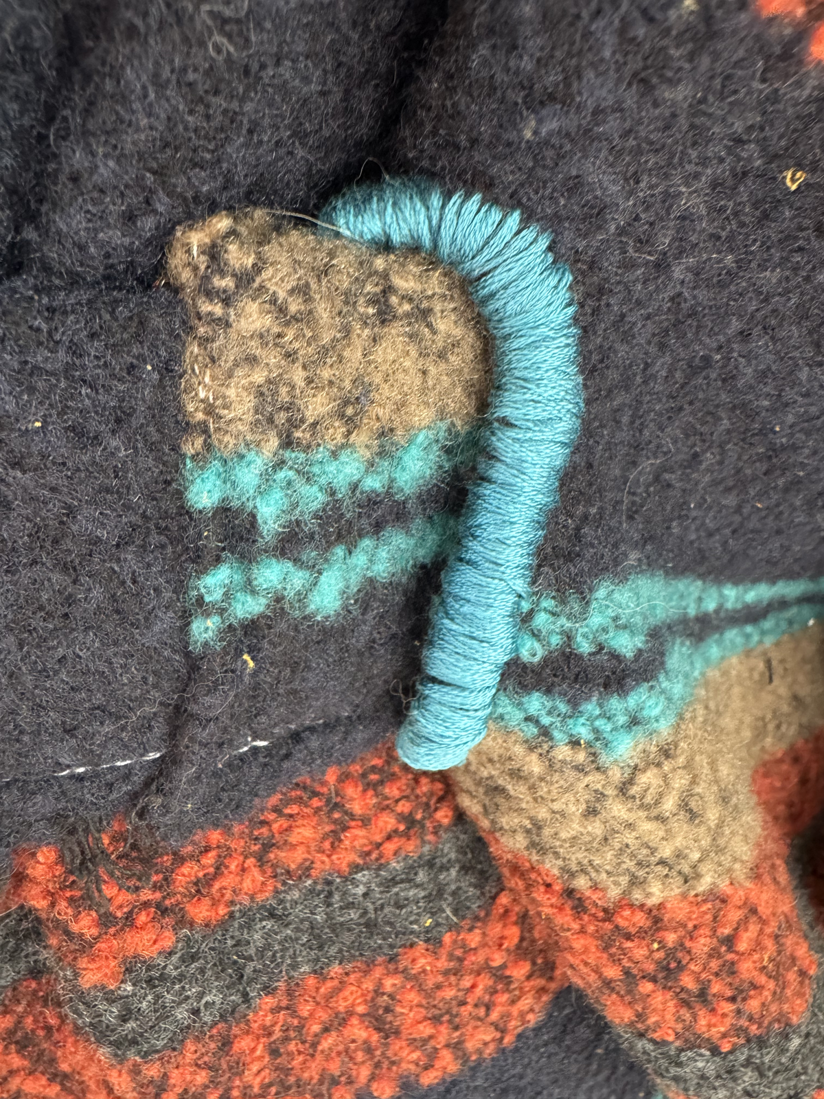 Close-up detail of teal thread-wrapped toggle on dark wool with terracotta and teal stripe