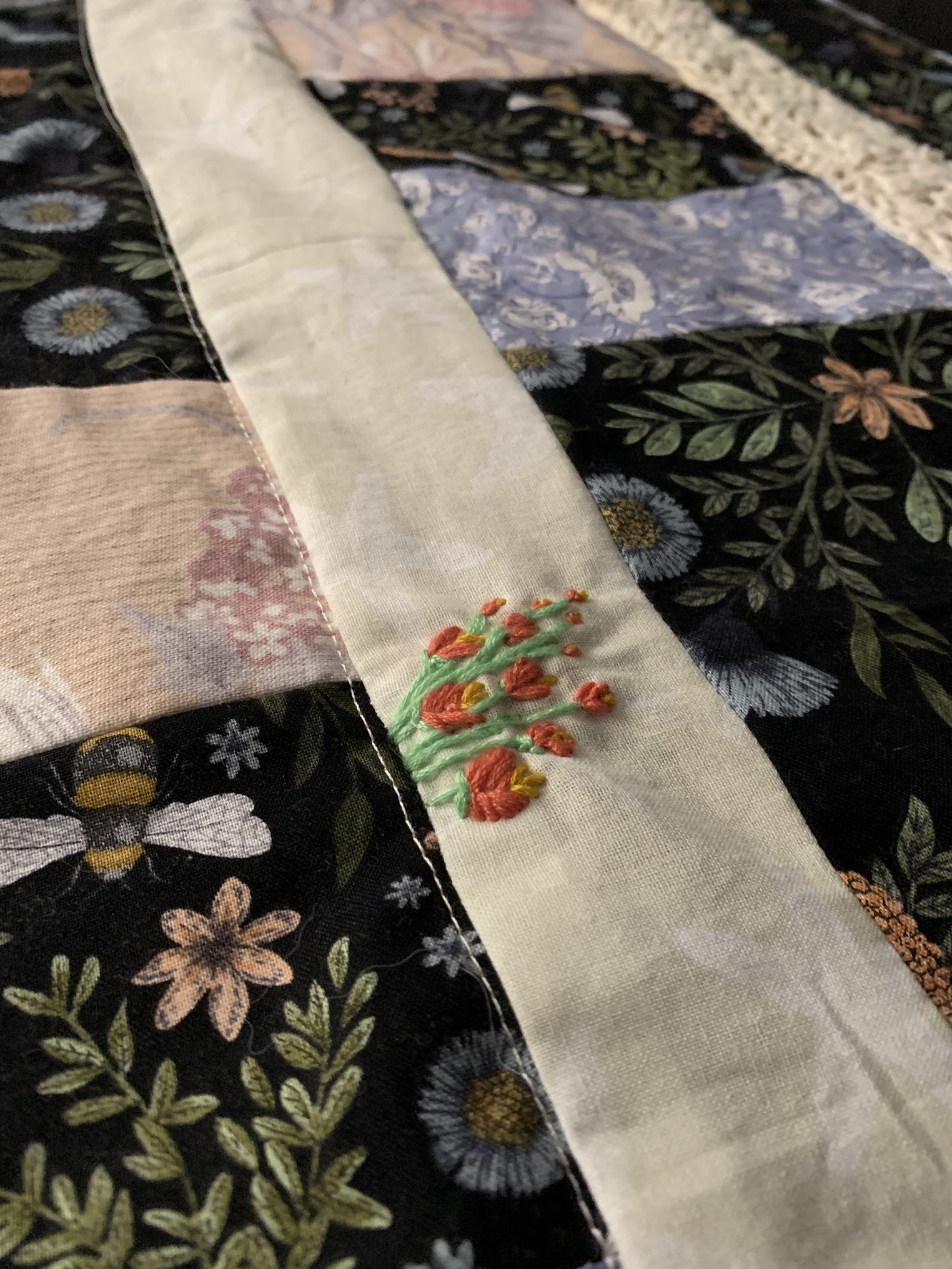 Close detail of Practical Magic quilt — small red and orange floral motif hand embroidered into the cream sashing strip