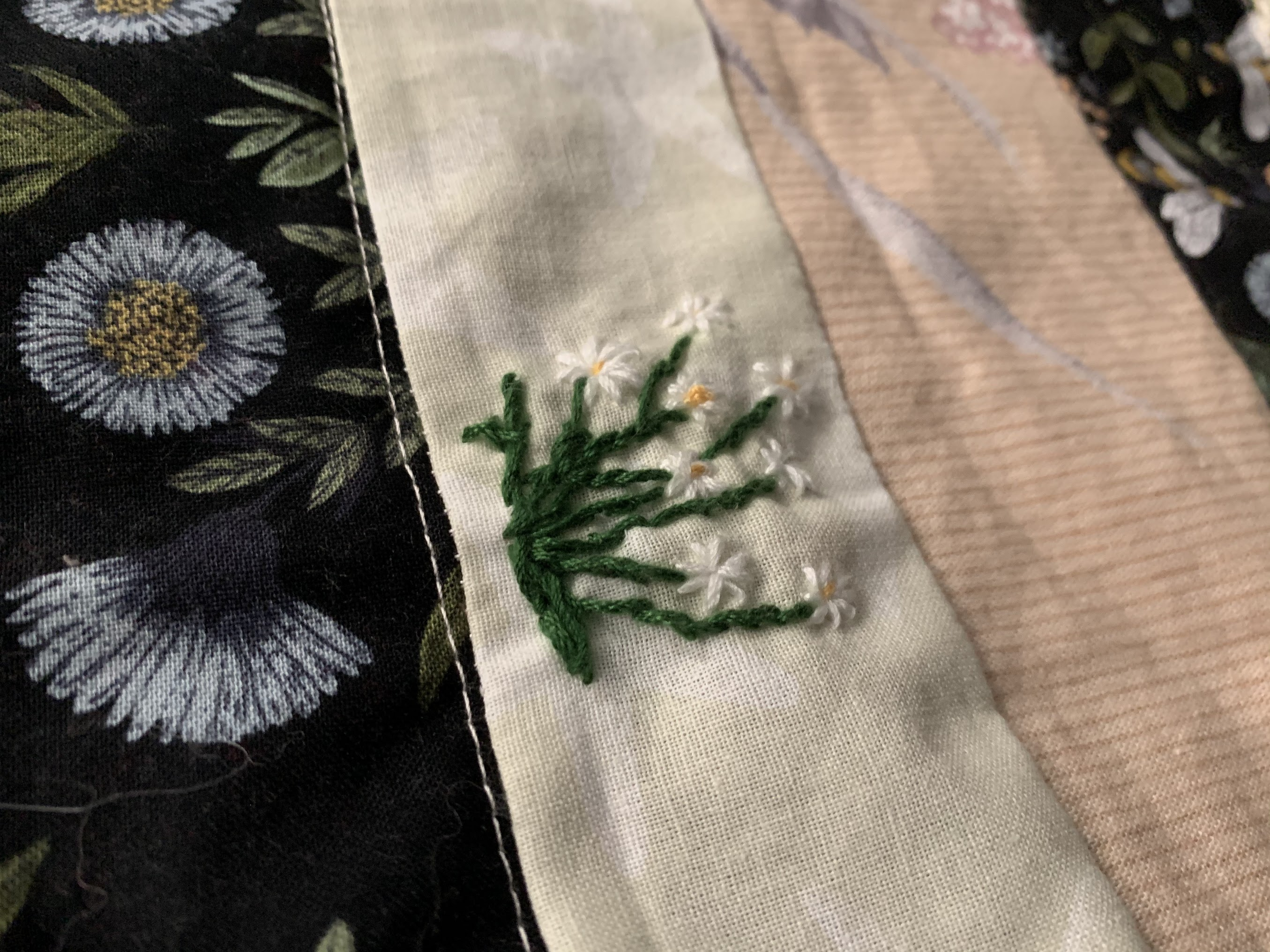 Close detail of Practical Magic quilt — white daisy cluster with green stems embroidered into cream sashing beside blue botanical print