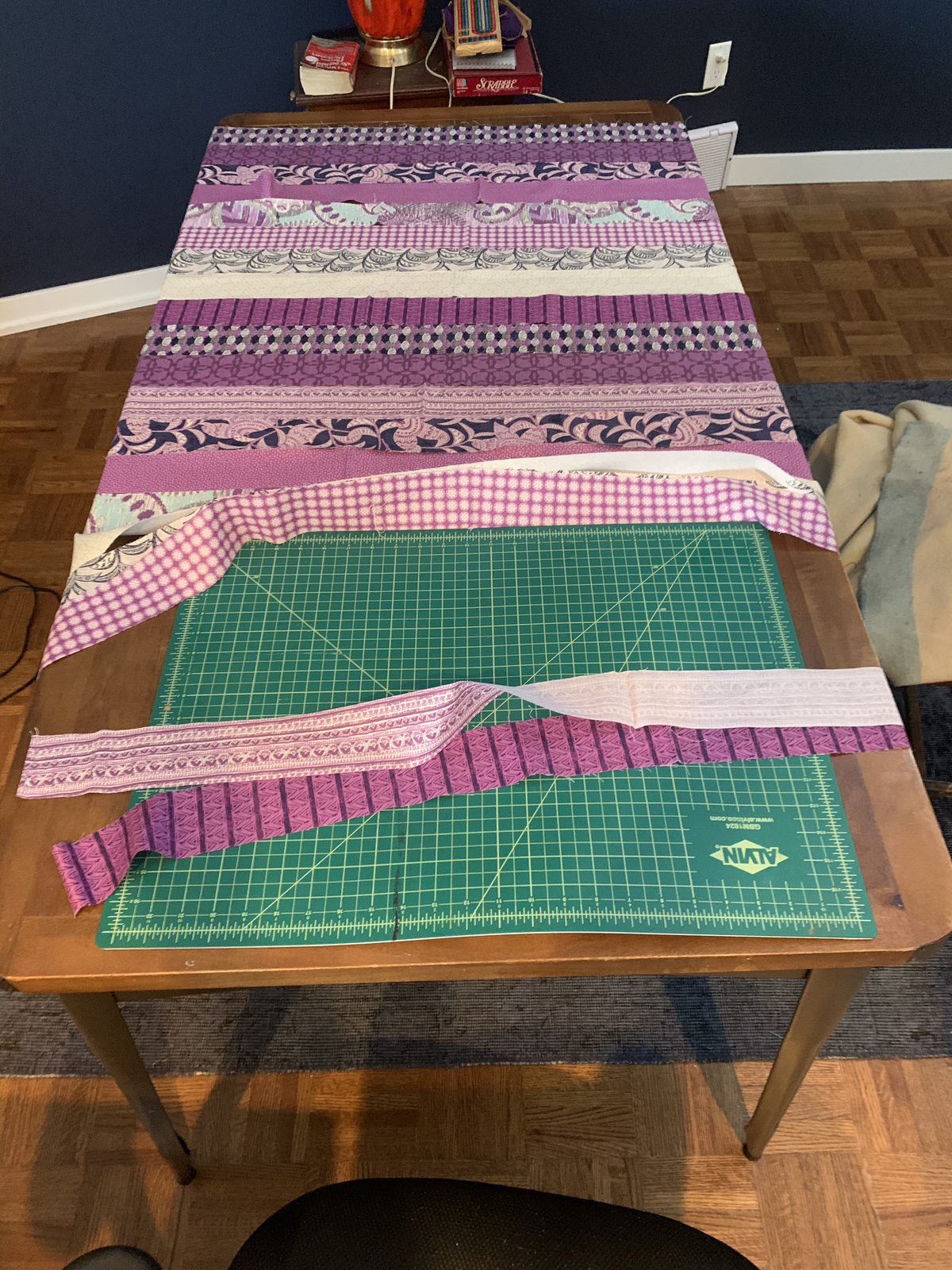 Purple Raining Prints strip piecing in progress — sewn rows of purple prints with cutting mat and loose strips