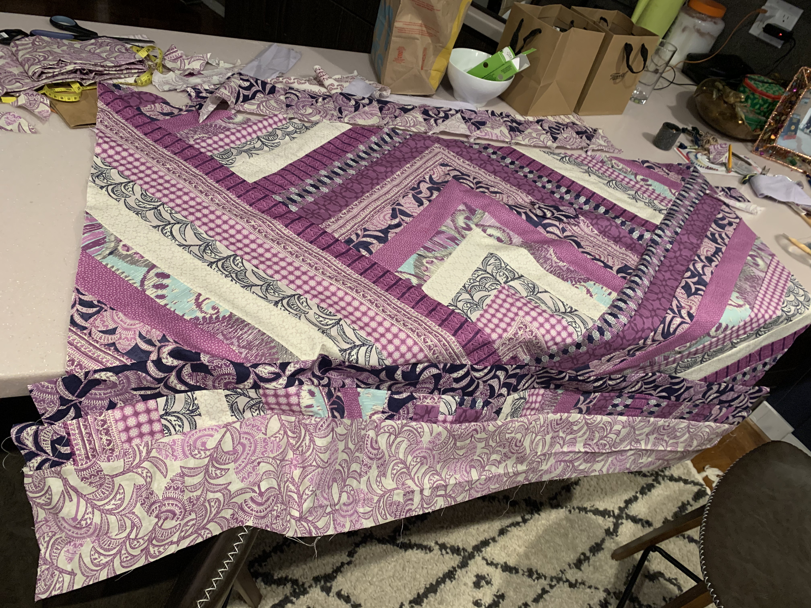 Purple Raining Prints quilt top draped on table — chevron pattern visible with purple paisley, gingham, and botanical prints