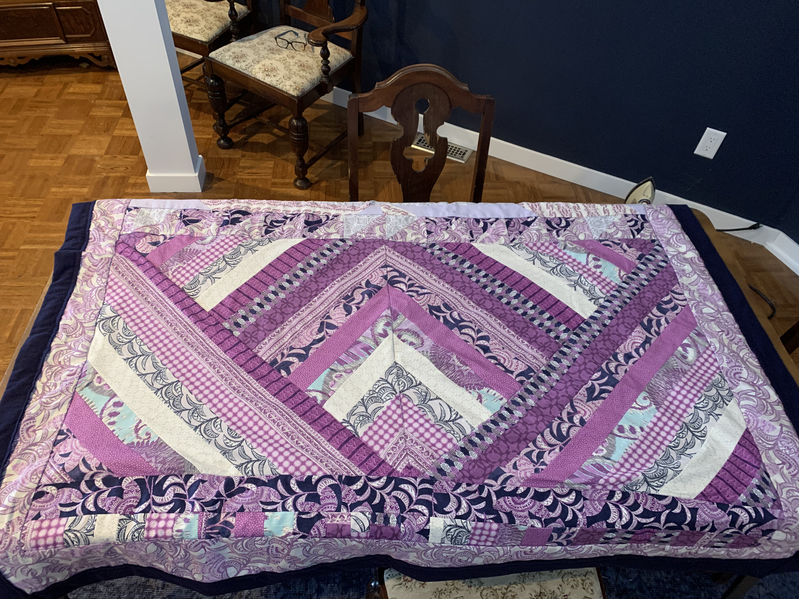 Purple Raining Prints quilt laid out — chevron strip design in purples, navy, lavender, and cream with dark navy binding