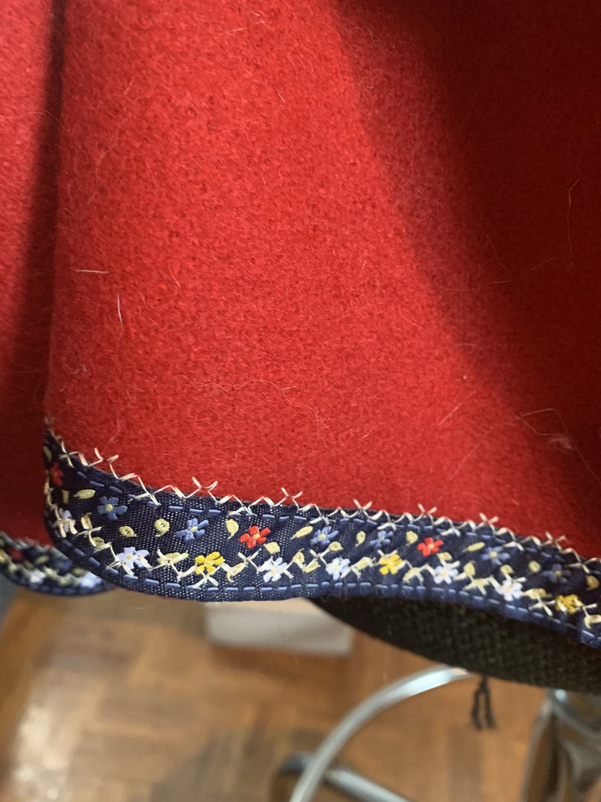 Close-up of embroidered hem on red wool — navy ribbon with hand-stitched flowers in white, yellow, and red