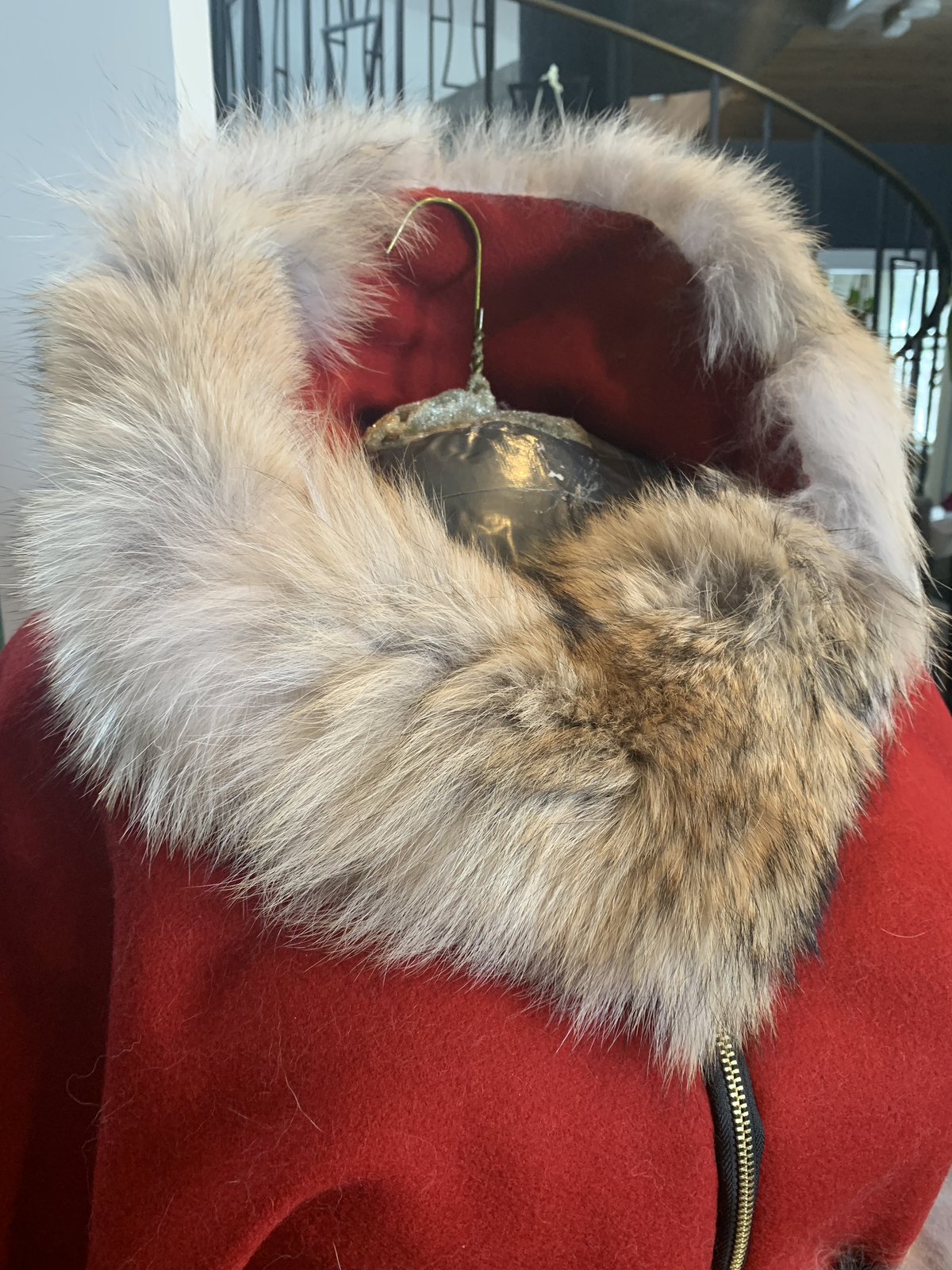 Close-up of coyote fur collar on the red cape — thick fur framing the hood with brass zipper visible