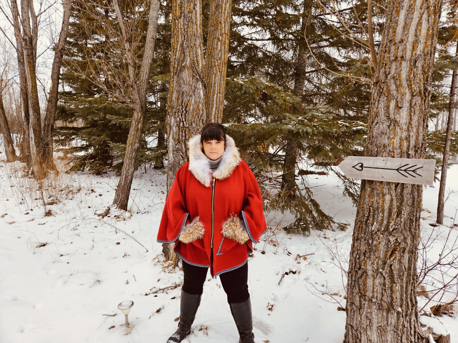 Marcella wearing the Red and Coyote cape outdoors in winter — red wool, coyote fur hood, snow and trees